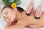 Close up of a beautiful woman enjoying a hot stone massage with a flower on her ear