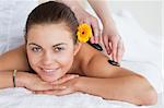 Smiling woman enjoying a hot stone massage with a flower on her ear