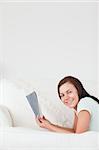 Portrait of a cute woman on a sofa holding a book looking at the camera