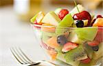 Fruit salad in a glass bowl, served on the table. Focus on blackberry. Natural light