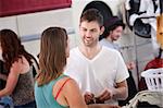 Handsome young Caucasian man talks with woman in laundromat