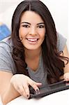 Beautiful happy young Latina Hispanic woman smiling, laying down and using a tablet computer or iPad at home on her sofa