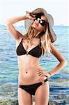 young woman wearing bikini and huge sunglasses poses like looking at the sun