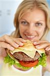 Mid Adult Woman Holding A Hamburger, Smiling At The Camera