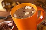 Hot chocolate with marshmallows in orange cup surrounded by chocolate and cookies (Selective Focus, Focus on the marshmallows in the middle of the hot chocolate)