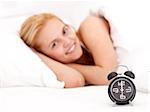 Alarm clock with a young woman lying in the bed at the background