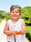 Little adorable girl posing with orange scooter in the park