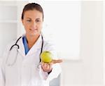 Good looking brunette doctor with stethoscope looking at an apple in the surgery