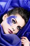 beauty shot of a model with purple glitter make up laying between purple silk sheets