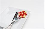 Chese and tomatoes on a white plate with a knife and fork on a white background