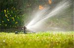 Lawn sprinkler spraying water over green grass in summer