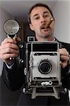 Photo of a retro 1940's style photographer taking a photo with an old 4x6 camera.  Photographer out of focus and camera in focus.