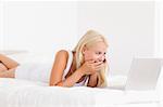 Woman laughing on the phone while using a laptop in her bedroom