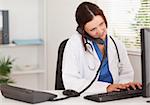 A female doctor is telephoning whilst typing on her keyboard