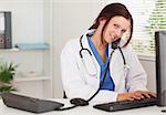 A female doctor is telephoning and typing in an office