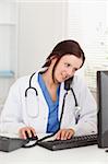 A female doctor is working with her pc in an office whilst telephoning