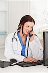 A female doctor is telephoning and looking to her pc