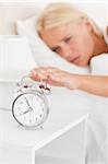 Portrait of a blonde woman awaken by an alarmclock with the camera focus on the object
