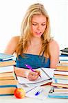 Young girl sitting at table with lots of books and doing homework
