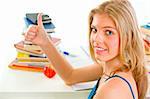 Smiling young girl sitting at table with books and showing thumbs up gesture