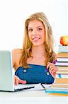 Smiling pretty young girl sitting at table with books and laptop