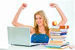 Smiling beautiful young girl sitting at table and rejoicing success