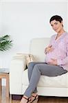 Pretty pregnant woman sitting on a sofa touching her belly in a waiting room