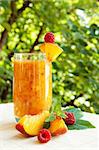 Peach cocktail in the garden in hot summer, sunny day with raspberries