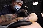 A tattoo artist applying his craft onto the leg of a female.