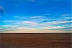 An empty field sits under beautiful skies with a wide open horizon at sunset.