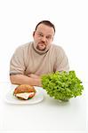 Diet choices concept - man with hamburger and lettuce at the table, isolated