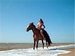 nude woman on horseback rides along the beach