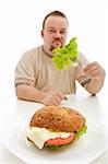 Diet choices concept - man reluctantly eating lettuce behind large hamburger