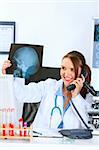 Smiling medical doctor woman talking on phone and holding patients roentgen