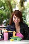 Young woman sitting outside eating noodles and smiling