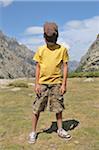 Boy with Hat Covering Face Standing in Mountainous Landscape