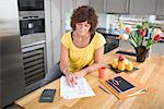 Woman sitting in kitchen doing paperwork