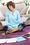 Uncertain woman sitting on floor with bills