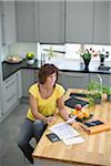 Woman sitting in kitchen with bills