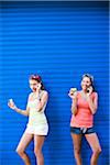 Two girls in front of blue wall, talking on phones
