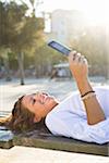 Fille couché sur le banc de parc, à l'aide de téléphone portable