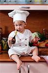 little boy in the cook costume at the kitchen sitting on the table