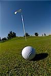 Image detail of golf ball in foreground with flag in background and deep blue sky