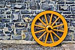 An old yellow wooden wagon wheel leaning against a stone wall
