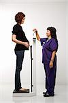 Pregnant Caucasian mid-adult woman being weighed by nurse.