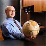 Caucasian middle-aged businessman sitting at desk in office holding globe.