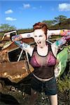 Sexy tattooed Caucasian woman yelling and holding her hands over her ears in junkyard.