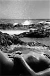 Young adult Caucasian female nude lying on rocky coast of Maui, Hawaii.