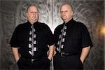 Caucasian bald mid adult identical twin standing together looking at viewer.