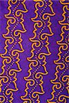 Close-up of purple vintage fabric with repetitive orange designs printed on polyester.